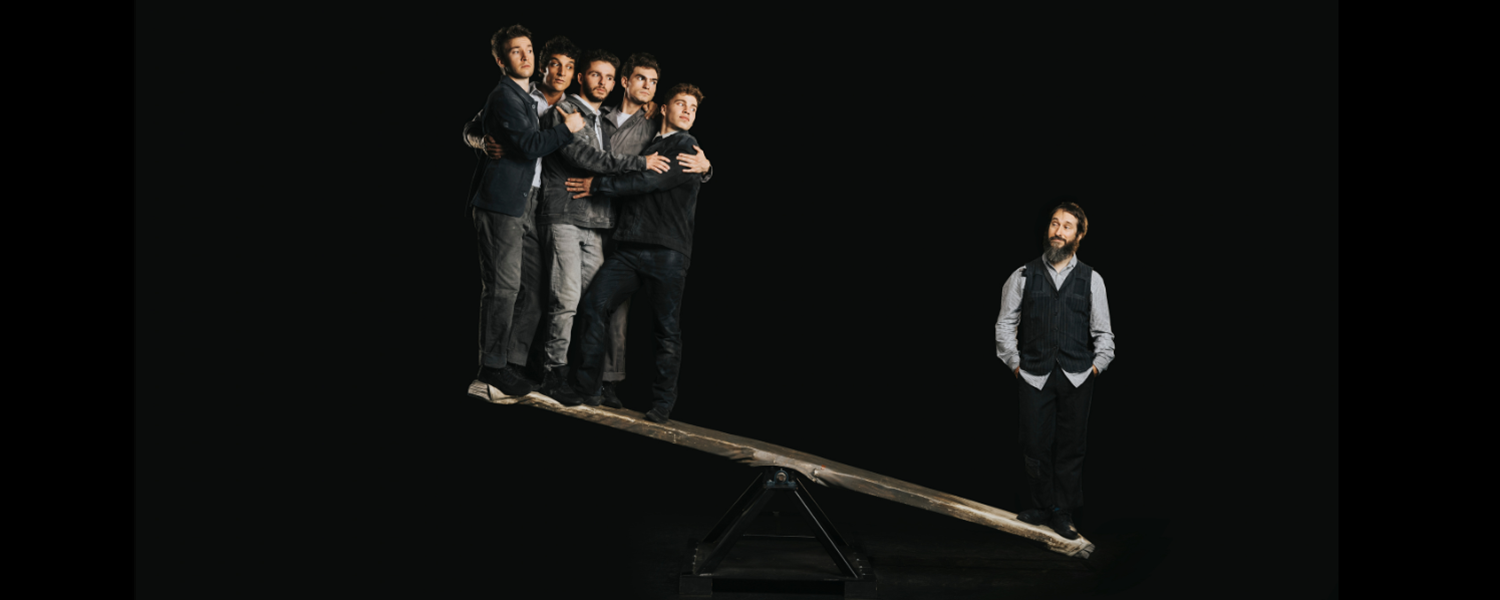 man suspended upsaide down on scaffolding structure with 3 bystanders looking on